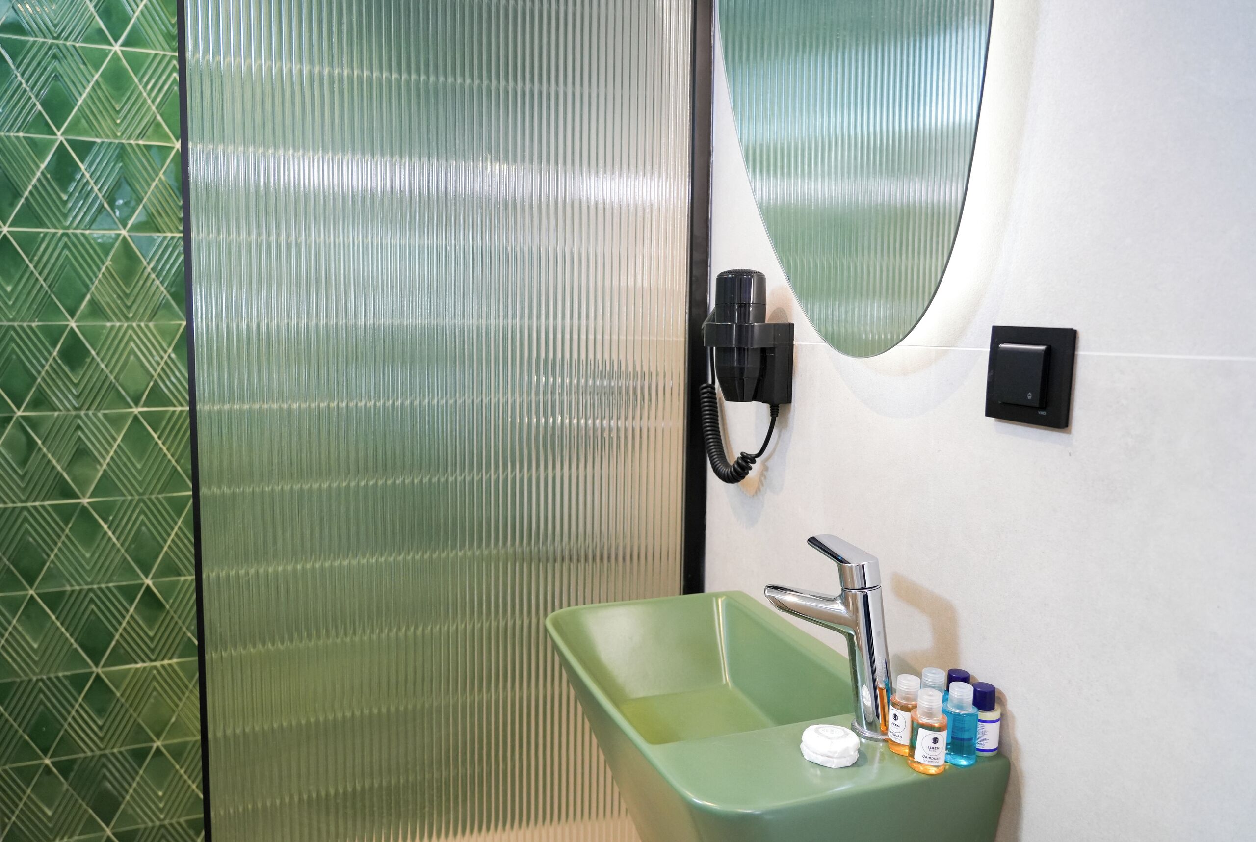 A bathroom with a green sink, a mirror, and a hand dryer.