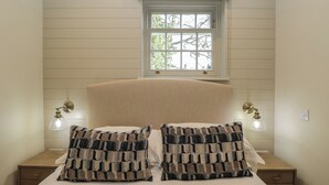 Ein Schlafzimmer mit einem Bett, zwei Nachttischen, einem Fenster mit blickdichter Vorhangbesatz und Wandleuchten.