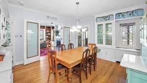 Ein Esszimmer mit Holztisch und -stühlen, einer Chandelierleuchtre und Blick auf einen Garten durch ein Fenster mit dekorativen Glasscheiben.