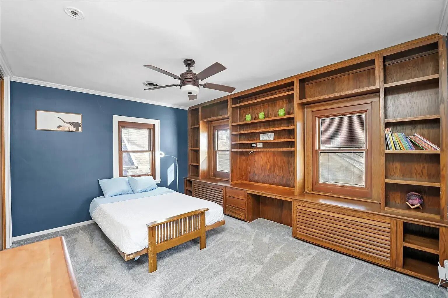A bedroom with a bed, a ceiling fan, a window, and built-in wooden shelving.