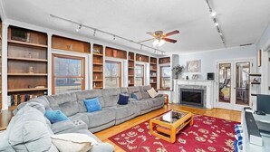 Ein Wohnzimmer mit grauem Sofa, Holzregalen, einem Kamin und einem Deckenventilator.