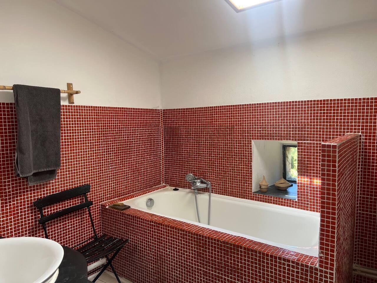 Casa de banho com parede em azulejos vermelhos, uma banheira, uma cadeira preta e um espelho.