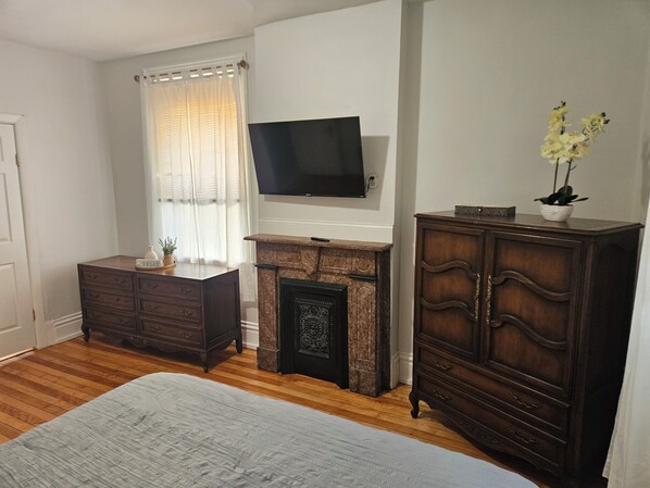 A bedroom with a bed, a dresser, a television, a fireplace, and a window with curtains.