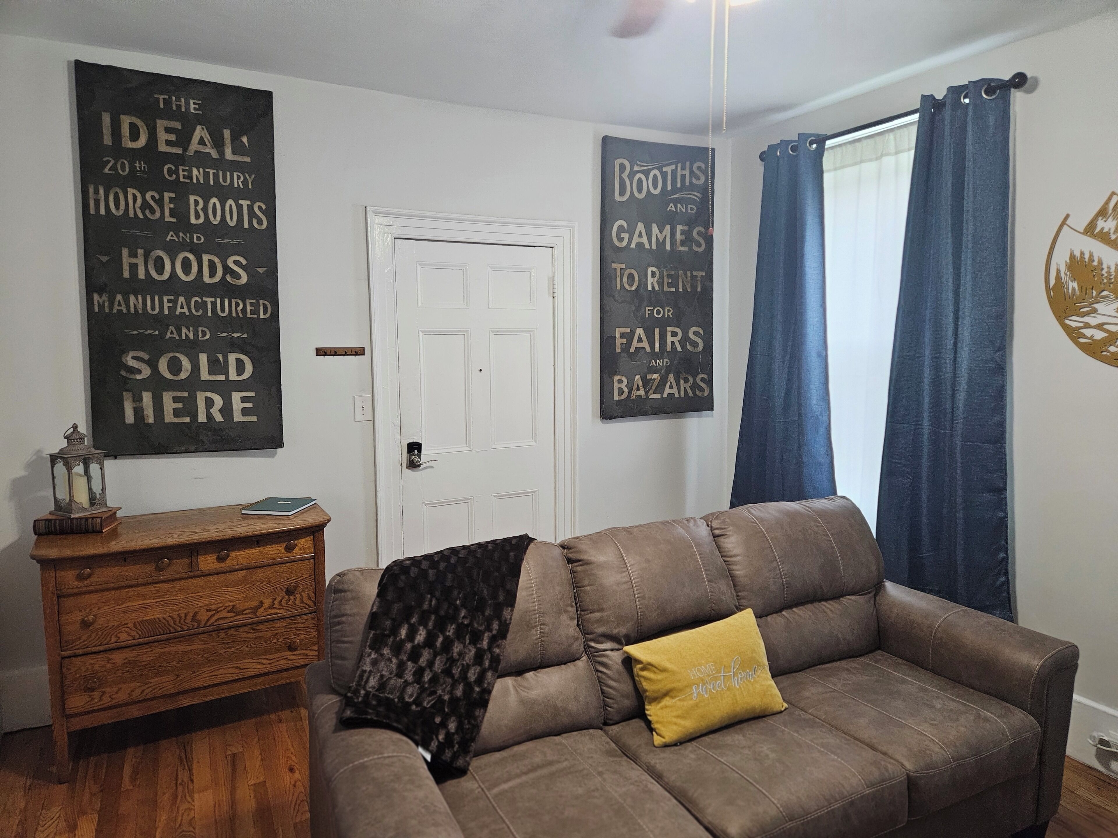A living room with a brown leather sofa, a wooden side table, and two wall decorations.
