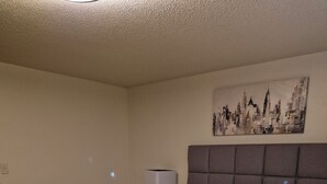 Una cama bien hecha con una colcha estampada, cabecera y una lámpara fijada a la pared.