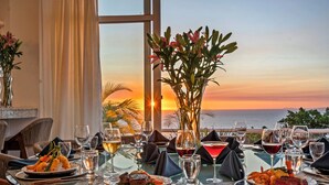 Una mesa preparada para la cena, con vistas al atardecer, platos de comida y copas de vino.