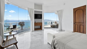 A modern hotel room with a balcony, a bed, a TV, and a view of the sea.