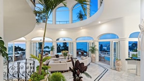Un interior amplio con techo curvo, una zona de estar con sofá y ventanas grandes que ofrecen vistas a la ciudad y al mar.
