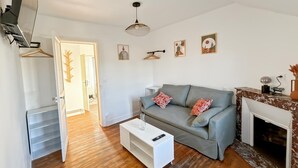 Ein Wohnzimmer mit grauem Sofa, weißem Couchtisch und Kamin. Eine Treppe führt in einen anderen Raum, darüber ein hängender Lampenleuchter.