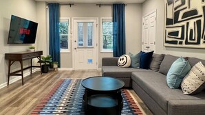 A living room with a grey sofa, a black coffee table, a TV mounted on the wall, and a large abstract painting.