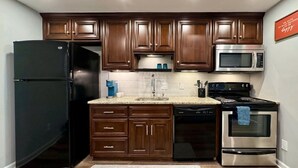 A kitchen with dark wooden cabinets, a black refrigerator, a stainless steel microwave, a dishwasher, and an oven.