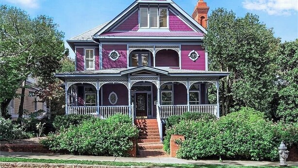 A two-story house with a gabled roof, a front porch with a railing, and a chimney.