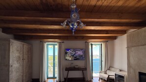 A room with wooden beams, a chandelier, a sofa, a fireplace, and a television. - Entre Ciel et Mer Hotel (Bonifacio)
