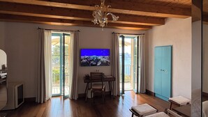 A room with wooden flooring, a chandelier, a television, a table, and a blue cabinet. - Entre Ciel et Mer Hotel (Bonifacio)