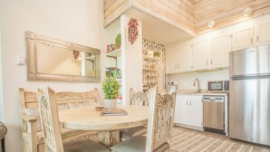 Een moderne keuken met witte kasten, een roestvrijstalen koelkast en een eethoek met een houten tafel en stoelen.
