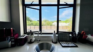 Une cuisine dotée d’un évier en acier inoxydable, d’une fenêtre donnant sur un espace verdoyant et de divers ustensiles de cuisine disposés sur le plan de travail.