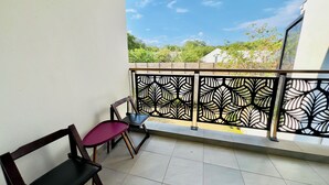 Un balcon avec deux chaises, une balustrade décorative et une vue sur la verdure et les bâtiments.