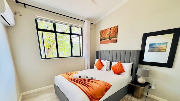 Une chambre d’hôtel moderne avec un grand lit, une fenêtre donnant sur des arbres, une tête de lit grise et deux tableaux accrochés au mur.