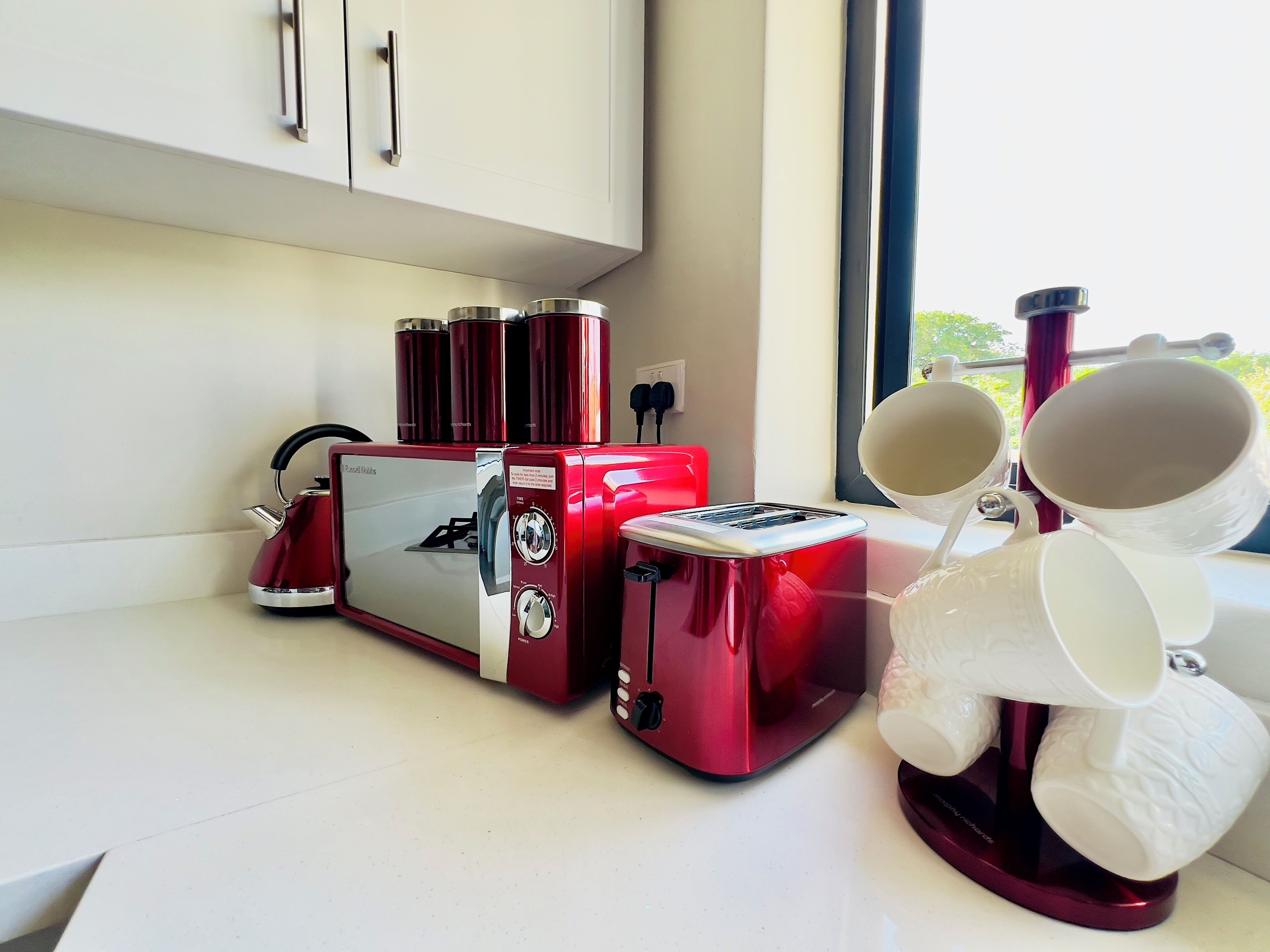 A kitchen with a red toaster, a kettle, and white mugs on a counter.