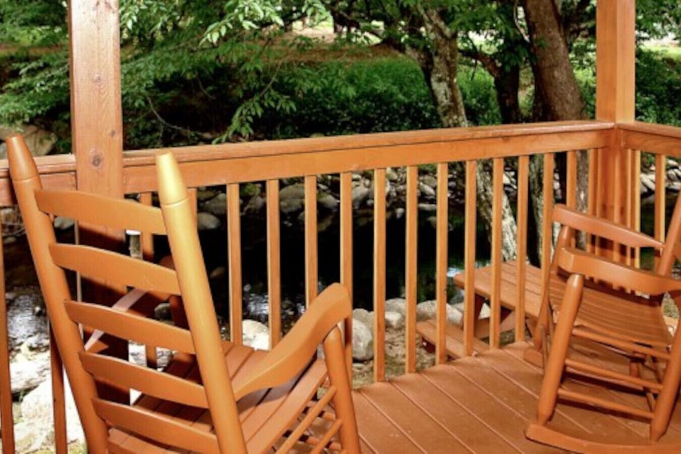A wooden deck with two rocking chairs and a stone wall in the background.