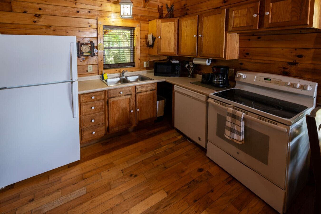 Una cocina compacta con armarios de madera, un refrigerador, un lavaplatos, una estufa y un microondas.