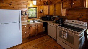 Eine kleine Küche mit Holzschränken, einem Kühlschrank, einer Spüle, einem Herd und einer Mikrowelle.