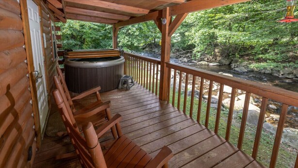 Eine Holzterrasse mit Whirlpool und Holzstühlen, mit Blick auf eine natürliche Landschaft.