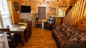 Ein gemütliches Blockhäuschen-Interieur mit einem Holzesstisch, Stühlen, einer Couch und einem an der Wand befestigten Fernseher.