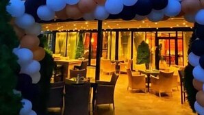 Un espace extérieur aménagé avec un patio couvert, doté de chaises et de tables, et décoré d’une arche de ballons.