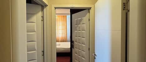 Pasillo de hotel con puertas numeradas 402 y 403, que conduce a una habitación con cama y ventana con cortinas.