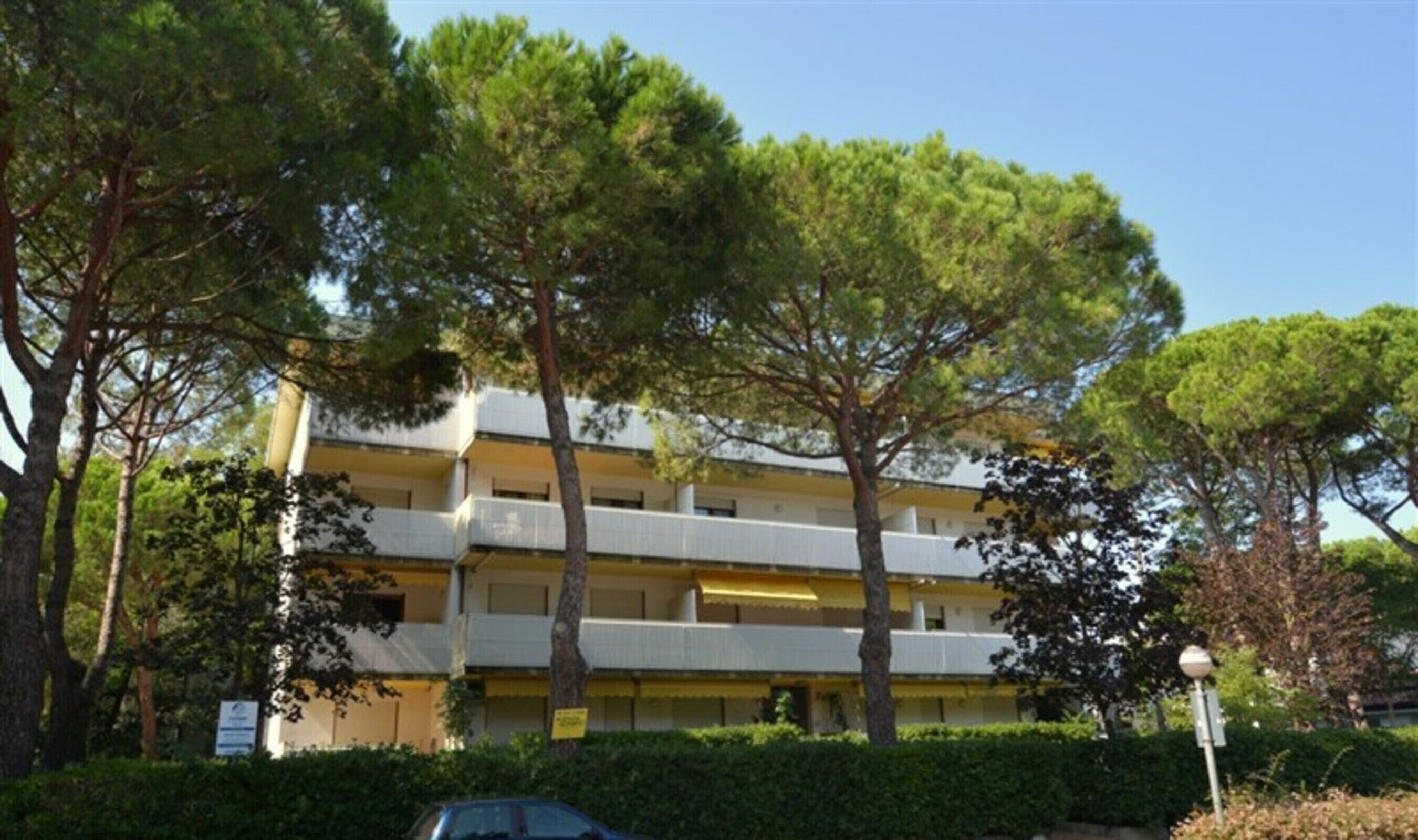 Un edifici de diverses plantes amb balcons, envoltat d'arbres i vegetació.