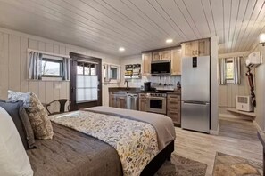 A compact RV interior with a kitchenette, a bed with a patterned bedspread, and a small seating area. - Valentine's Cabin w/WiFi • Scenic Views • Walk to Downtown • Fireplace (Bryson City)