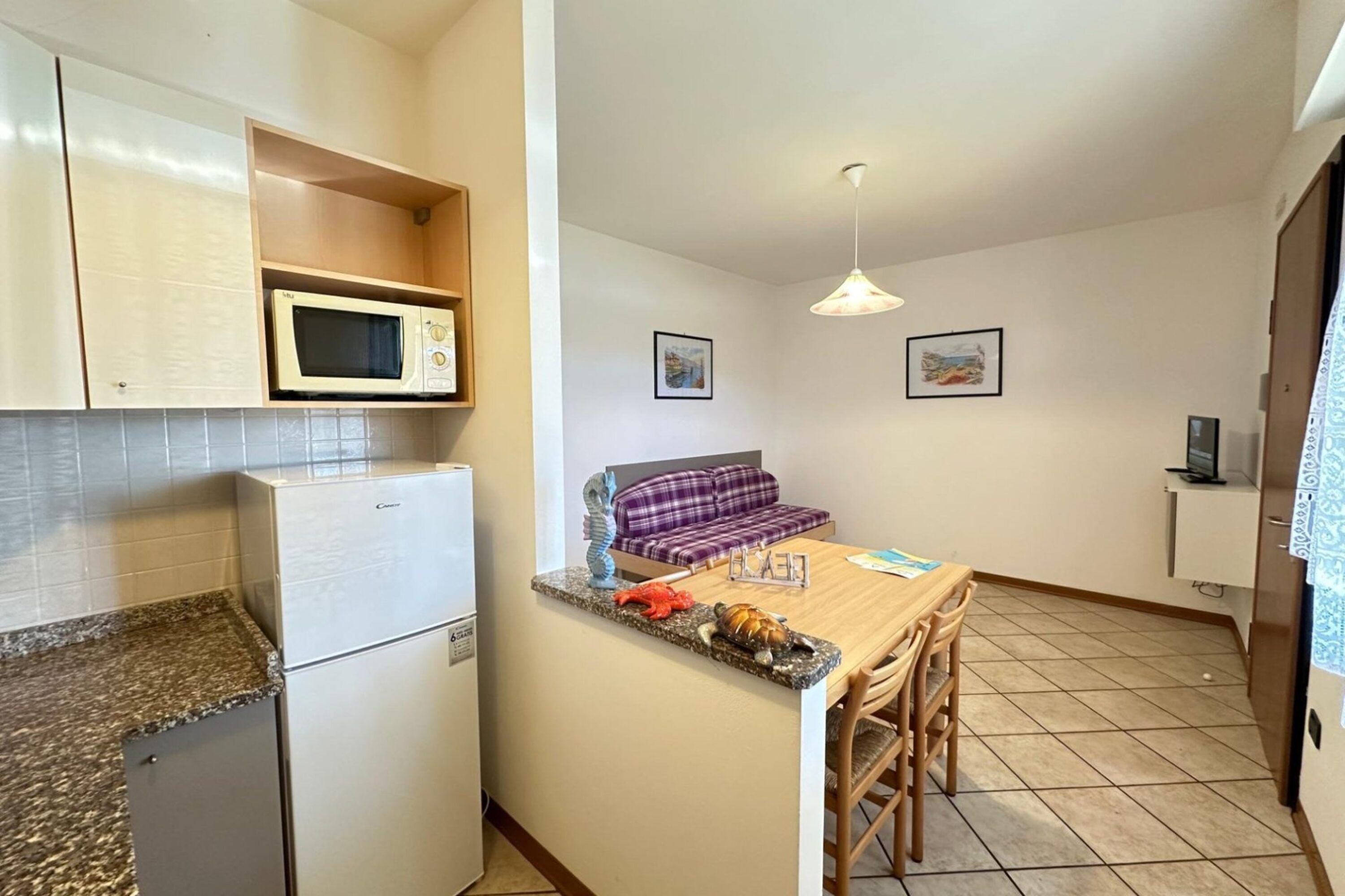 A compact kitchen with a microwave, refrigerator, and granite countertop. A dining area with a table and chairs is adjacent to the kitchen.