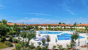 Ein Hotel mit mehreren Schwimmbecken, einem angelegten Garten und einer Reihe von Gebäuden mit gelben Fassaden und roten Dächern.