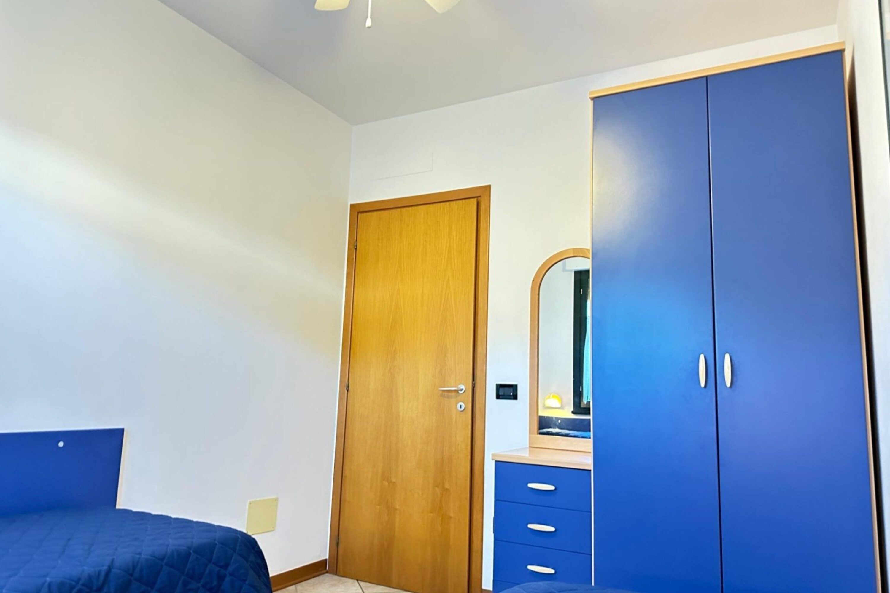 Un dormitorio con puerta de madera, un armario azul, un espejo y una cama con cabecera azul.