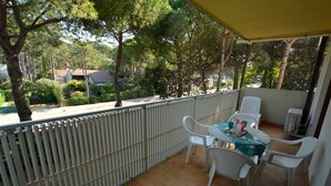 A covered outdoor patio with a table and chairs, surrounded by a metal fence and trees. - Cozy Residence Near the Beach in Lignano (Lignano Sabbiadoro)
