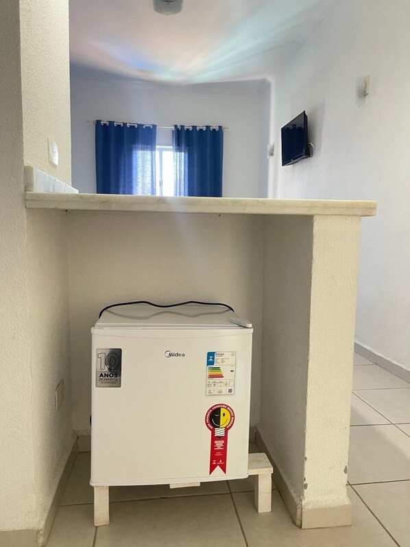 A compact kitchenette with a white refrigerator, a small countertop, and a power outlet. - Pousada Píer 22 (Caraguatatuba)