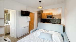 Ett kompakt hotellrum med en säng, en TV som är monterad på väggen, ett litet pentry med mikrovågsugn och en liten sittgrupp.