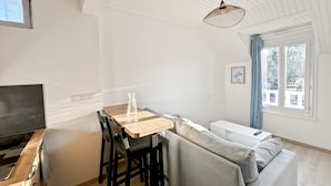 Ett modernt och kompakt vardagsrum med en matplats, en soffa, en TV och ett fönster med gardiner.