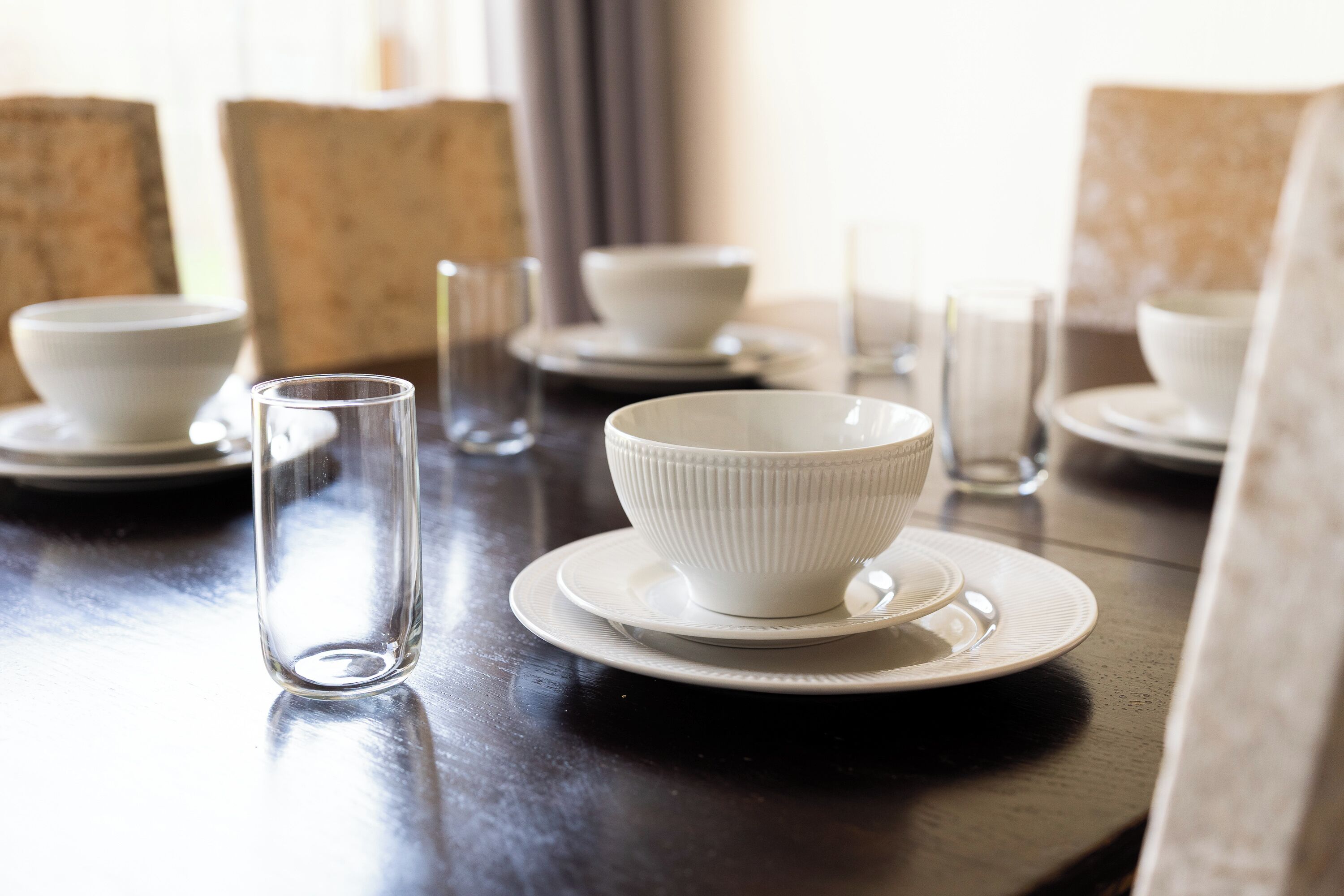 Una mesa de comedor con fuentes, platos y una copa blancos.