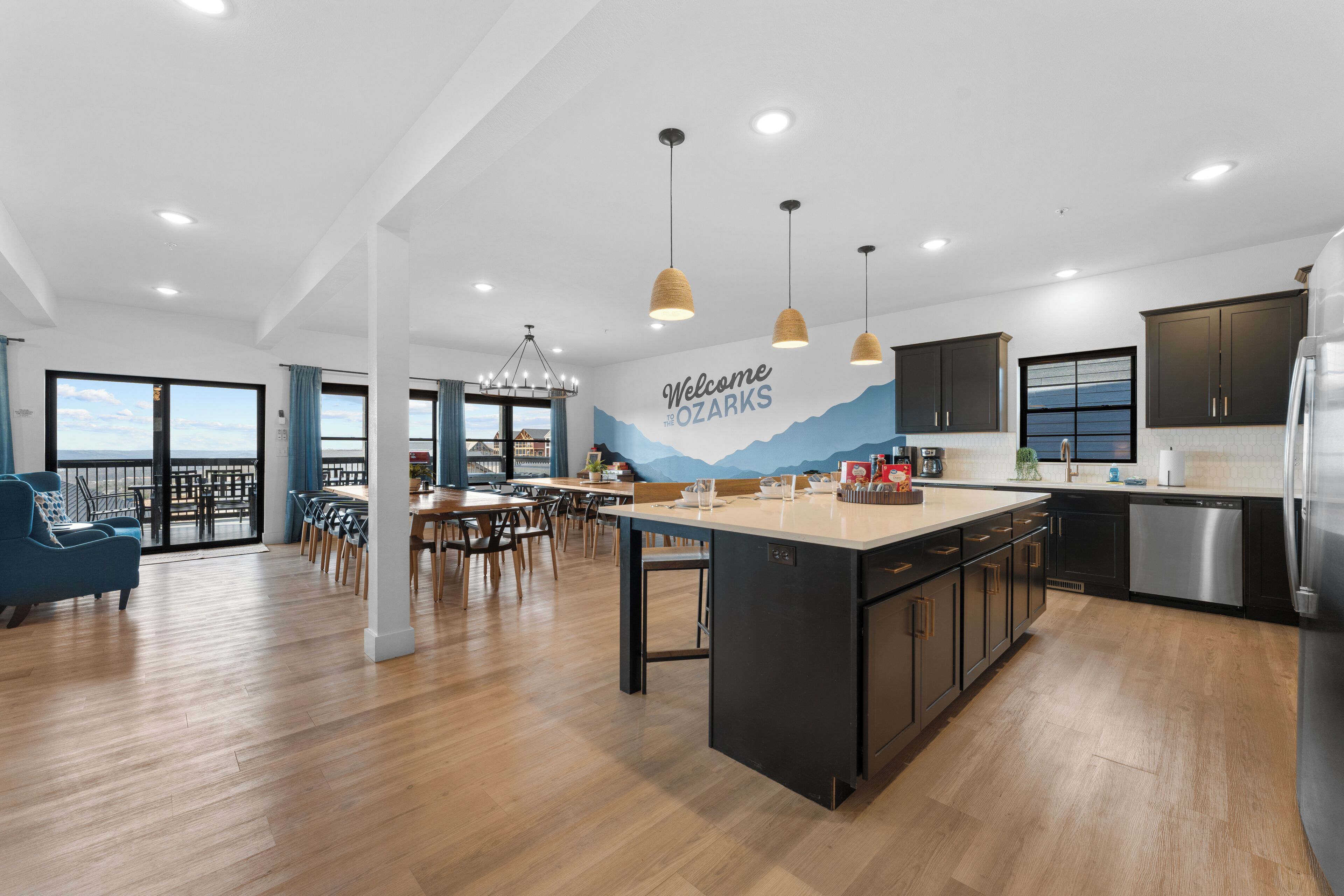 A modern kitchen with a central island, black cabinets, stainless steel appliances, and a mural with a mountain view.