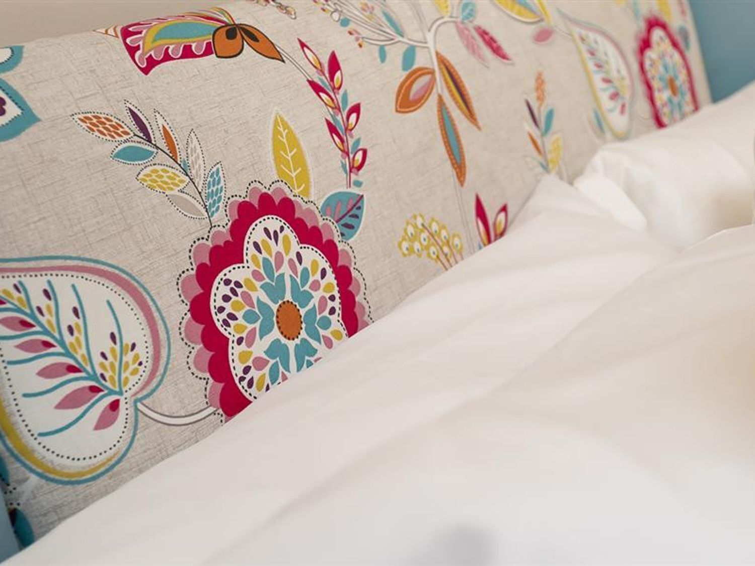 A bed with a floral-patterned pillow and a white comforter.
