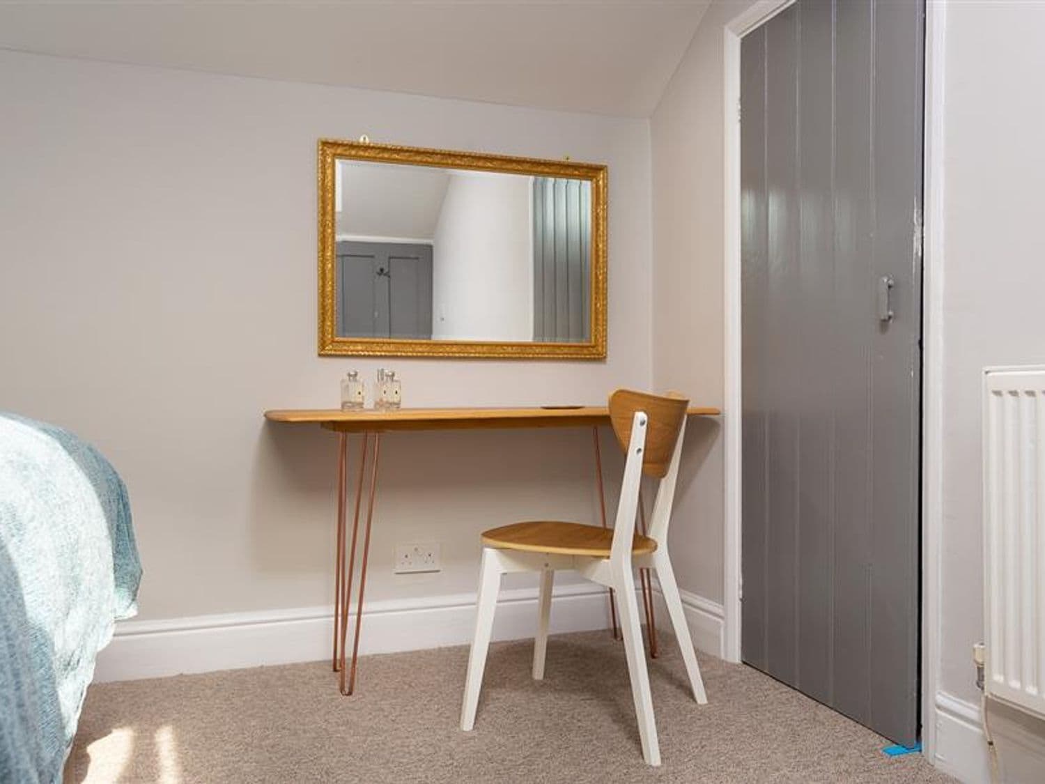 A small, neatly organized bedroom with a single bed, a desk with a chair, a mirror, and a door.