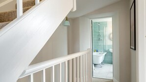Eine Treppe führt zu einem Badezimmer mit einer Duschkabine aus Glas und einer weißen Badewanne.