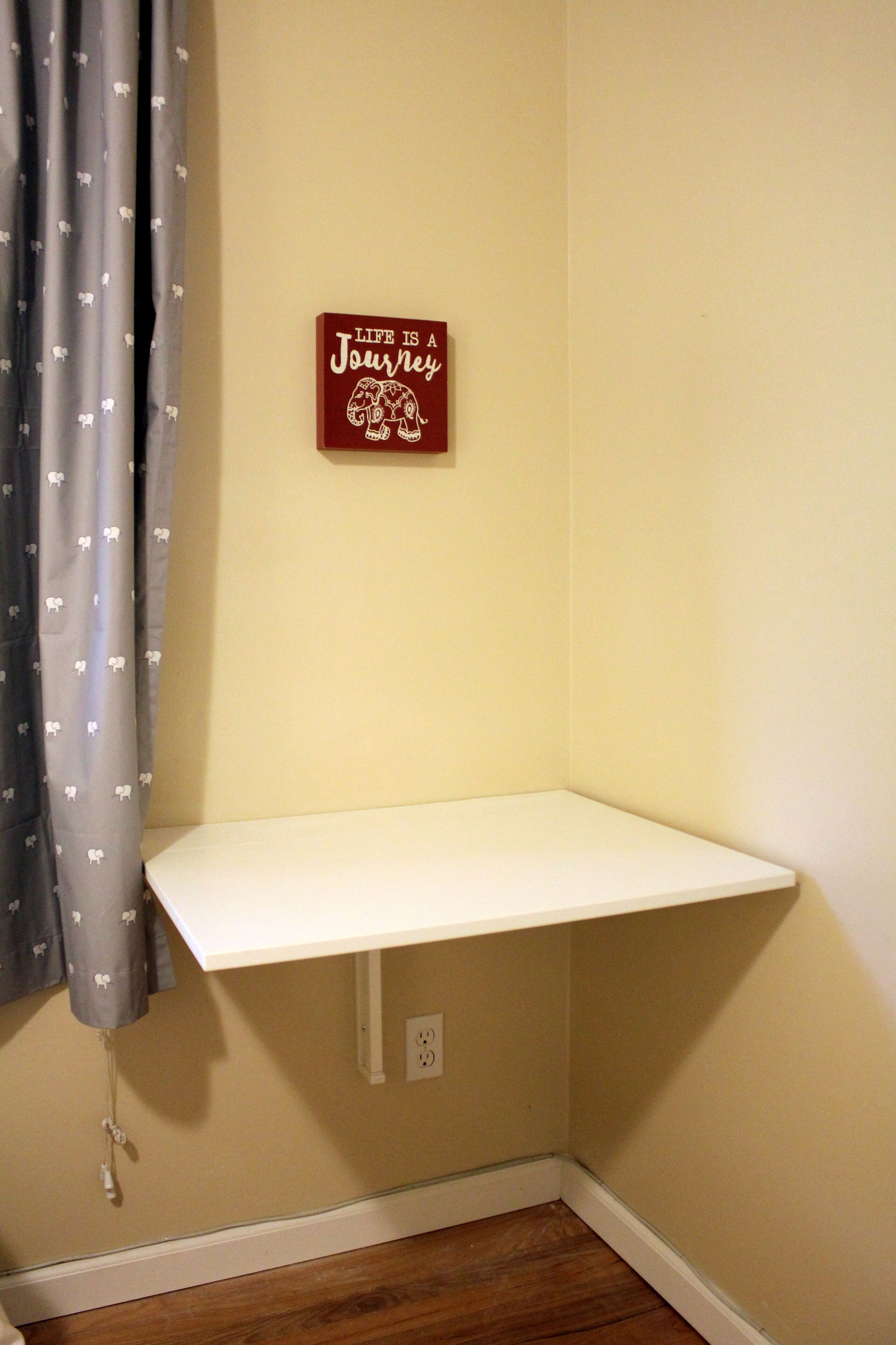 A corner with a white shelf, a wall-mounted sign, and a curtain with a pattern.