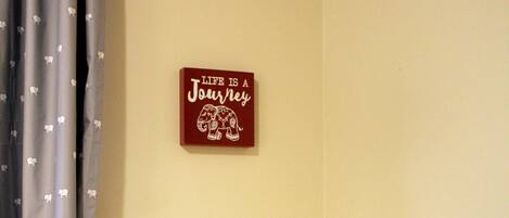 A corner with a white shelf, a wall-mounted sign, and a curtain with a pattern.