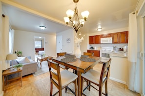 A dining area with a wooden table, chairs, a chandelier, and a kitchen in the background.