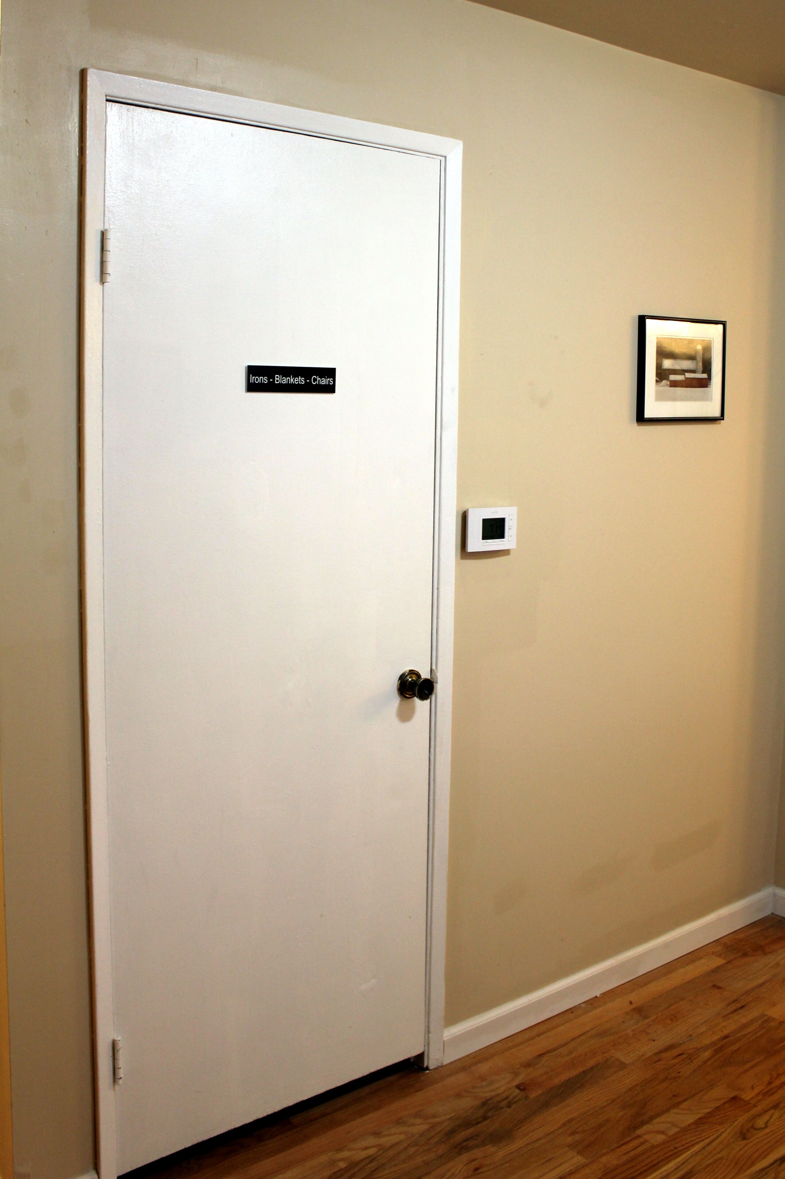 A white door with a sign reading "Irons - Blankets - Chairs" and a thermostat on the wall.