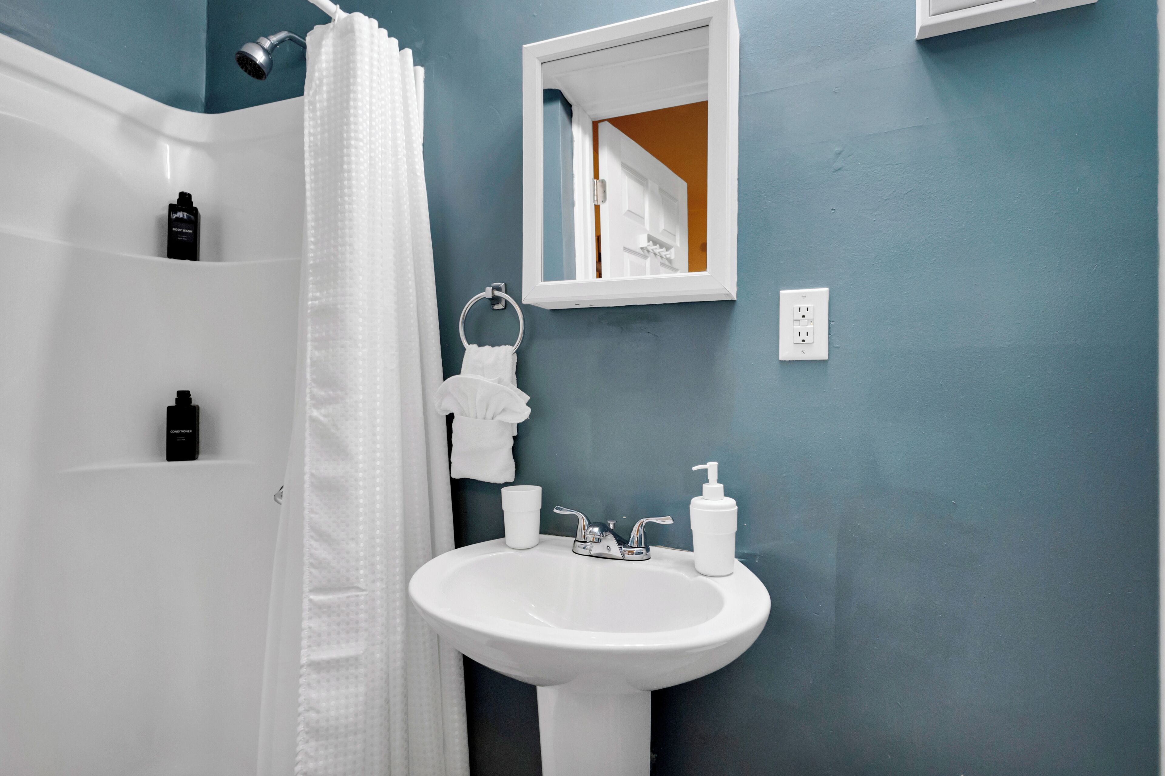 Een badkamer met een wit wastafel, een spiegel, een douche en een handdoekrek.