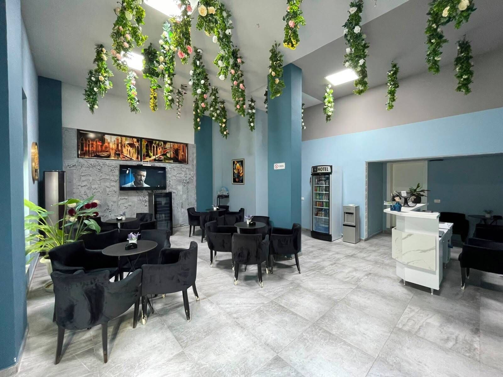 A hotel lobby with a modern design, featuring a seating area with round tables and chairs, a reception desk, and a wall-mounted television.